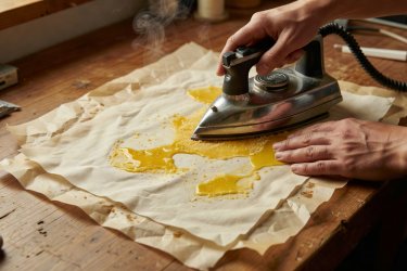 Parchment paper sandwich being pressed with a hot clothes iron to infuse yellow beeswax into cotton fabric