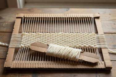 Cardboard frame loom with cotton warp strings and thick undyed wool weft woven through