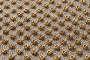 Close-up of golden embroidery thread forming neat French knots on natural oatmeal linen